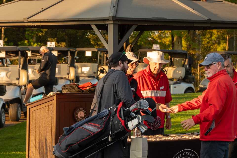 Golf tournament check-in under a tent with staff at a branded registration table.